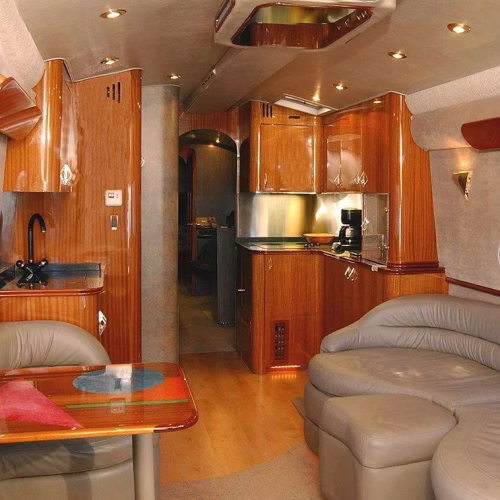 A cozy interior of a modern RV, featuring wooden cabinetry, a comfortable seating area, and a small kitchen equipped with appliances. The warm lighting enhances the inviting atmosphere.