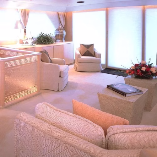 A cozy, elegantly designed living space featuring light-colored furniture, soft lighting, and decorative plants, creating a warm and inviting atmosphere. A stylish coffee table and floral arrangement add to the decor.